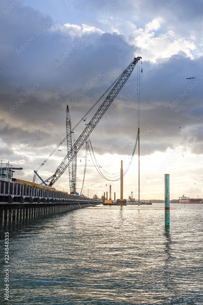 Drilling cranes at harbourside dock against cloudy sky
