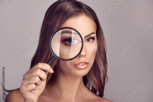 face portrait of woman looking through magnifying glass and increasing her eye