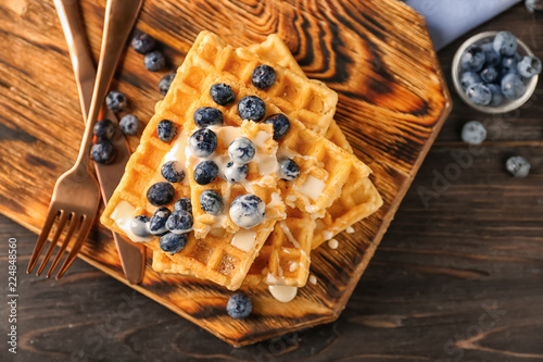 Delicious waffles with sauce and blueberries on wooden board