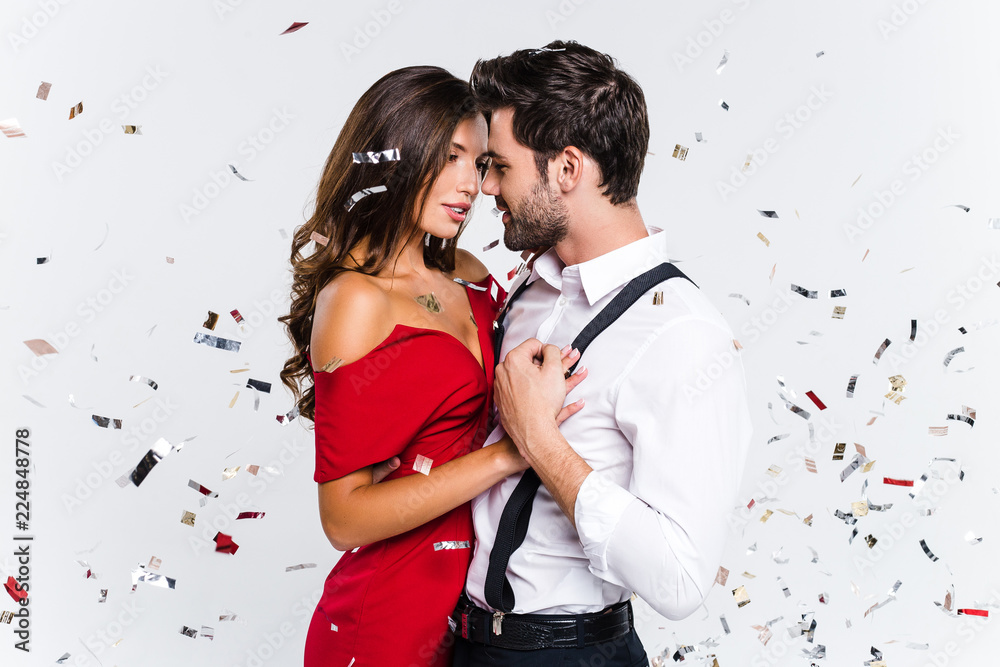 Heart to heart. Young beautiful couple dancing while standing against white background with confetti  - obrazy, fototapety, plakaty 