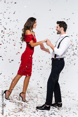 Teach me how to dance! Full length of young beautiful couple dancing while standing against white background with confetti 