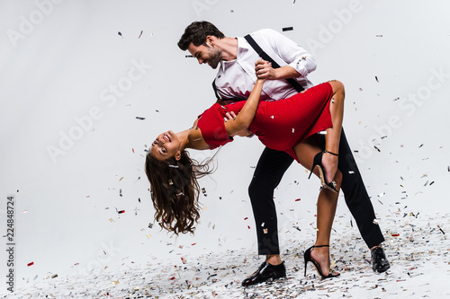 Fototapeta Naklejka Na Ścianę i Meble -  It is hot salsa! Full length of young beautiful couple dancing while standing against white background with confetti 