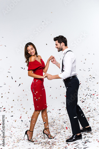 Perfect celebration for two. Full length of young beautiful couple dancing while standing against white background with confetti 