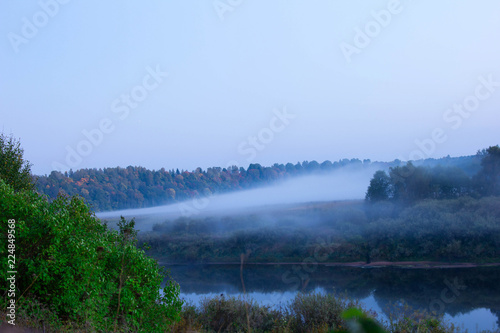 Amazing scenery of a river bank and field with starting fog. Evening landscape 