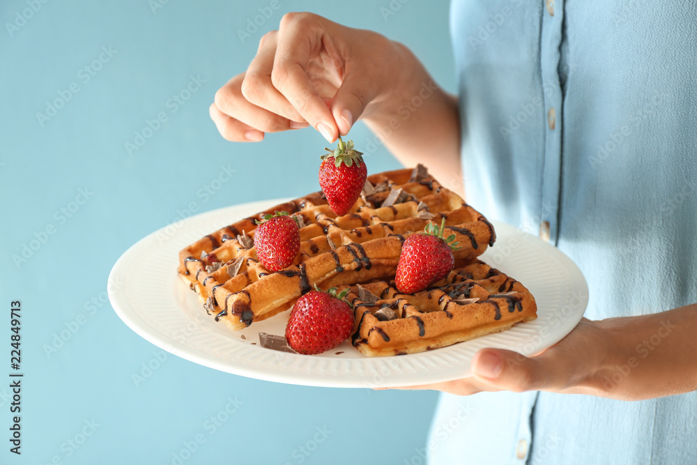 Woman holding plate with tasty waffles and berries on color background, closeup