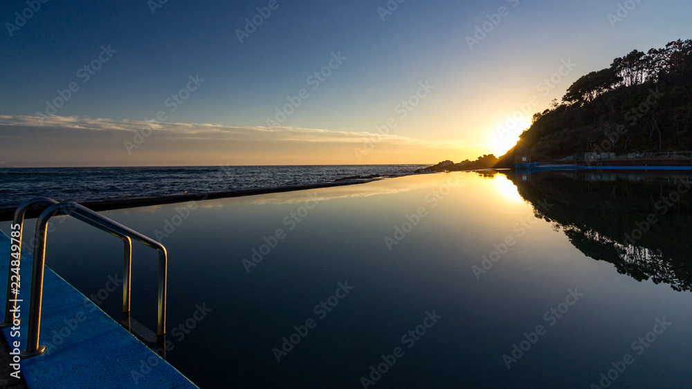 Obraz premium Sun rising over ocean baths with reflection in water