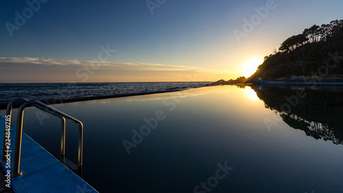 Sun rising over ocean baths with reflection in water