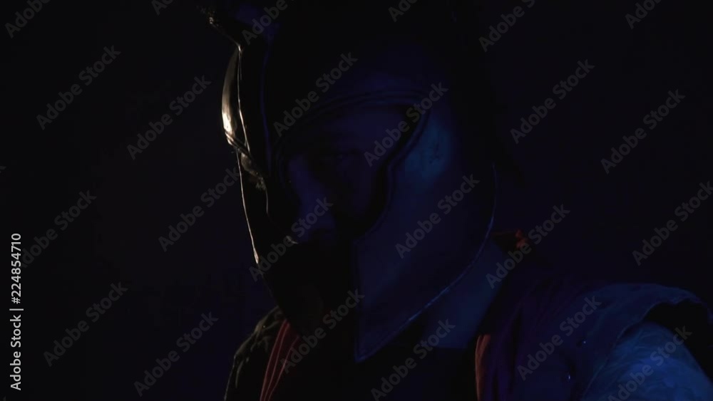 Male legionnaire in helmet slowly turns on camera in dark, slow motion Male legionnaire in helmet slowly turns on camera in dark, slow motion