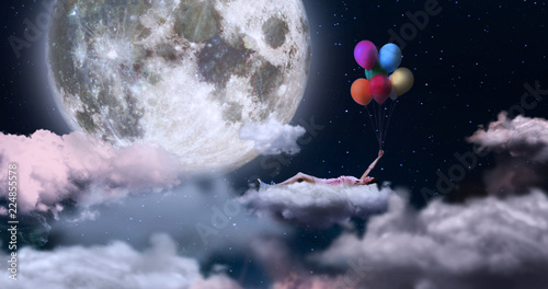 A woman holding on to colored balloons, flying in the sky lying on a cloud. On the sfin a giant moon. Concept of: dreams, freedom. photo
