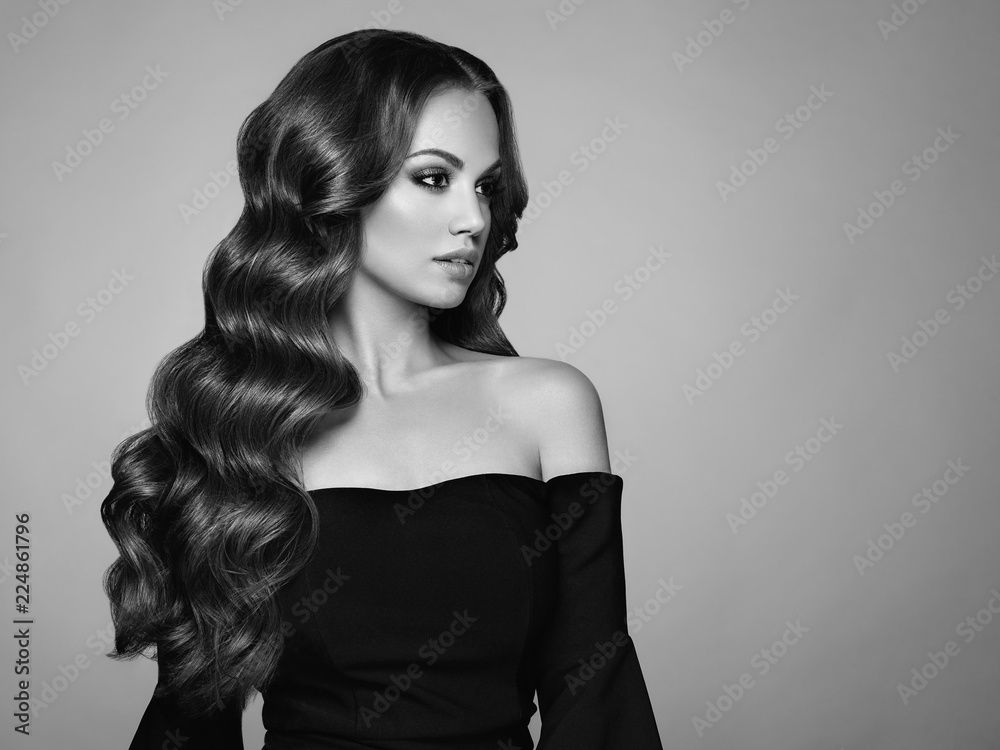 Fototapeta premium Brunette Girl with Long Healthy and Shiny Curly Hair. Care and Beauty. Beautiful Model Woman with Wavy Hairstyle. Make-Up and Black Dress