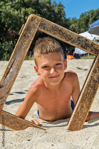 Pretty boy on beach with wooden picture frame