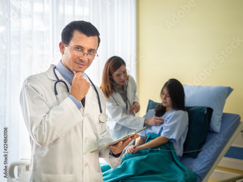smiling male doctor wearing a stethoscope and female doctor and patient discussing something while sitting at bed background.
