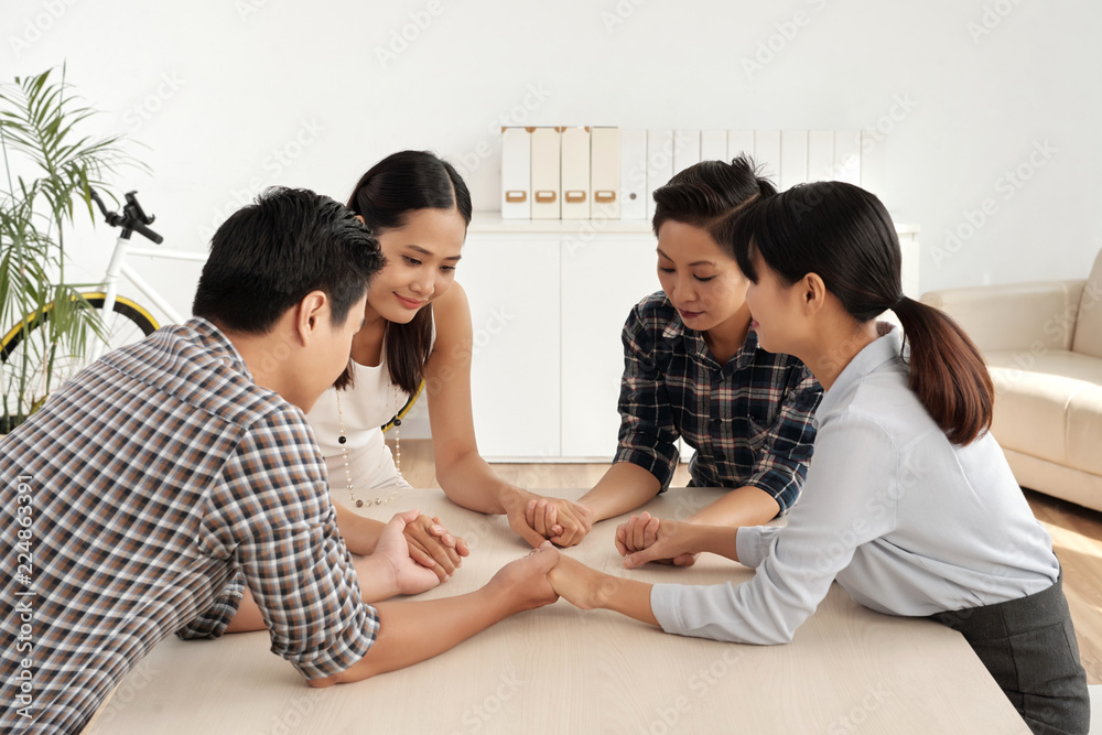 Group of smiling business executives holding hands and meditating together before difficut working day Group of smiling business executives holding hands and meditating together before difficut working day