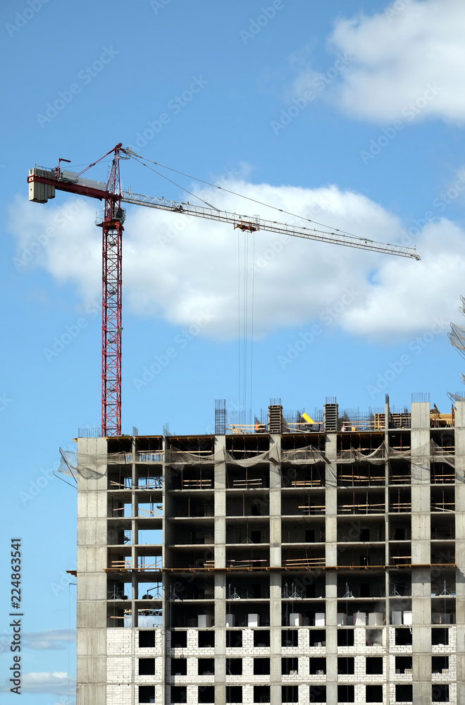 Big hoisting tower crane and top section of modern construction building in a city over blue sky with white clouds