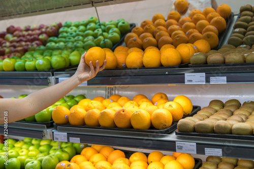 Fresh healthy fruits on shelves in supermarket. With a woman hand choosing best fruits