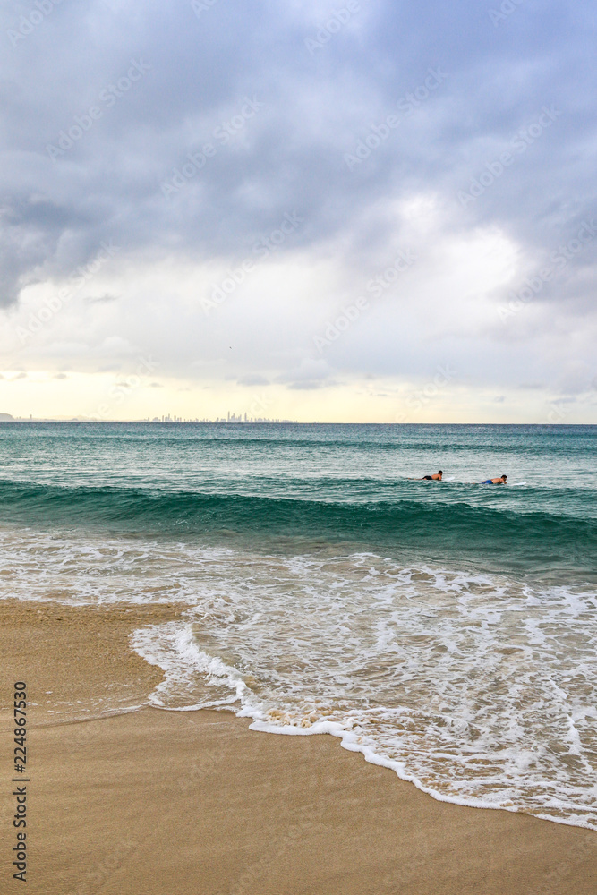 Surfers waiting to catch a wave against ocean and cloudy sky