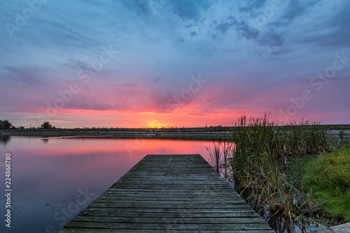 Colourful sunrise over timber jetty and lake
