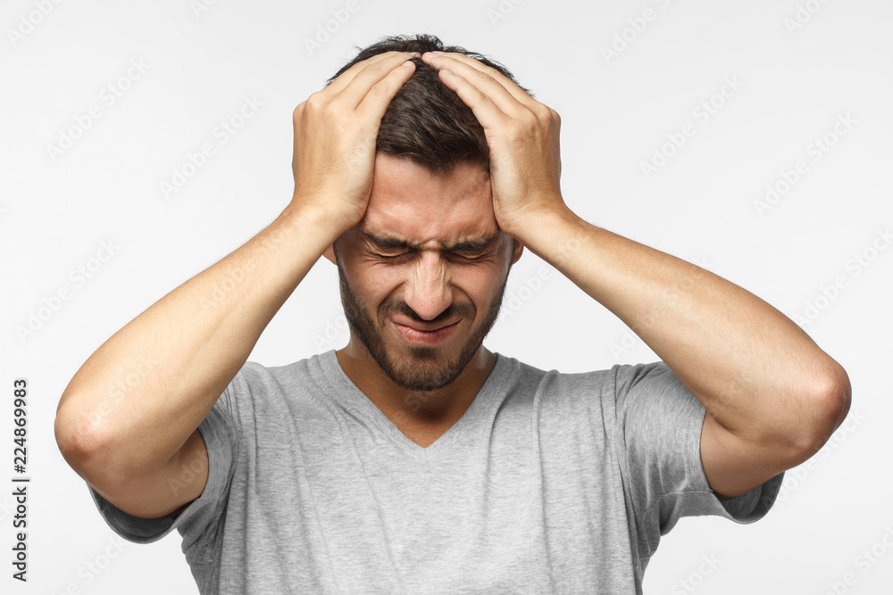 Headache concept. Upset unhappy young man squeezing head with hands. People, stress, tension and migraine concept Headache concept. Upset unhappy young man squeezing head with hands. People, stress, tension and migraine concept