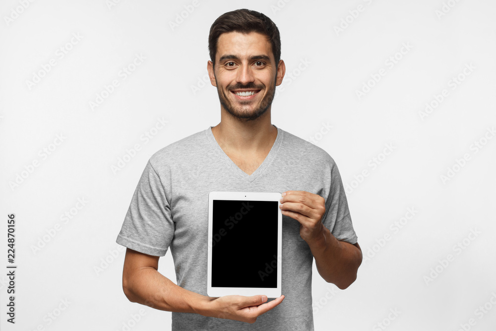 Young man presenting vertical blank tablet screen to viewers with smile, copy space for advertisment of goods or app,  isolated on gray background