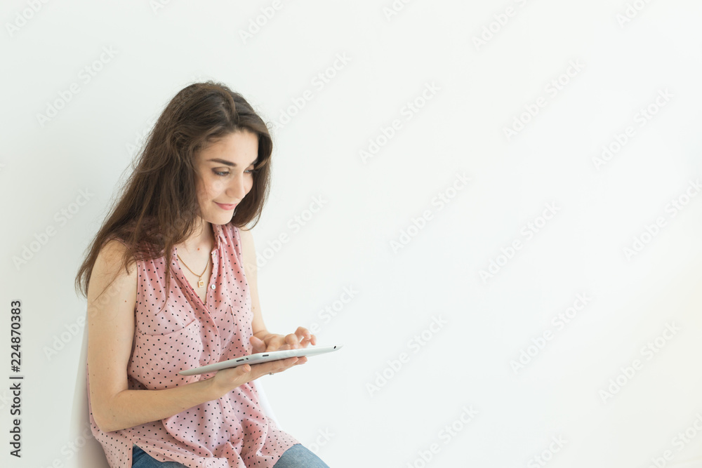 Technologies, emotions, people concept - young happy woman with tablet in her hands smiling over white background with copy space Technologies, emotions, people concept - young happy woman with tablet in her hands smiling over white background with copy space