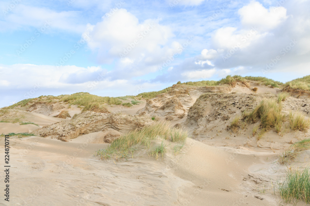 Dune valleys with deep wind holes carved out by heavy storm with swaying marram grasses with scattered clouds against blue sky