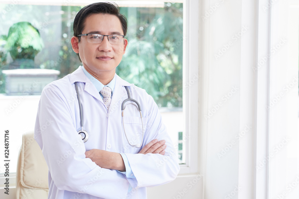 Portrait of male doctor in lab coat standing with arms crossed at hospital Portrait of male doctor in lab coat standing with arms crossed at hospital