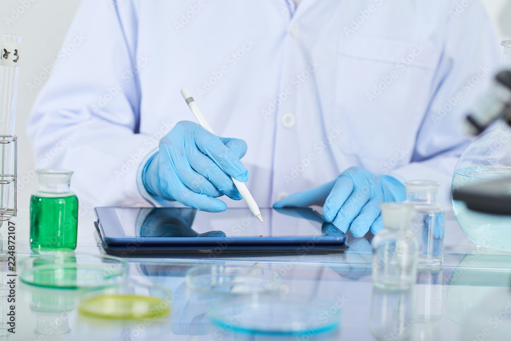 Fototapeta premium Close-up of chemist in protective glove using digital tablet in his work at lab