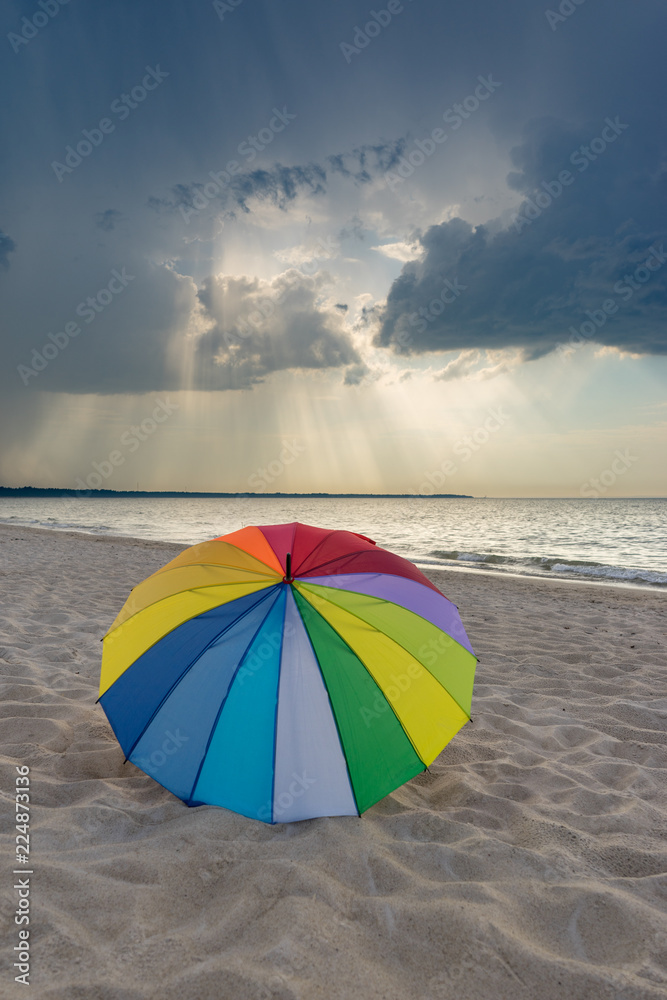 Multicolored umbrella on the beach against clouds