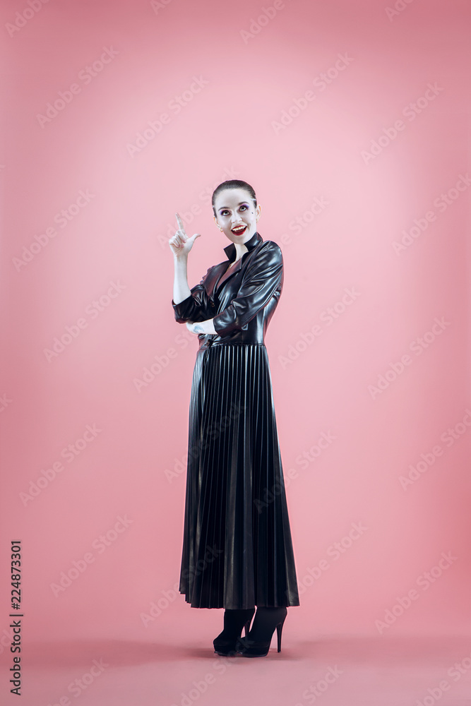 Halloween. Beautiful woman with bright black halloween makeup in a black leather cloak at pink studio Halloween. Beautiful woman with bright black halloween makeup in a black leather cloak at pink studio