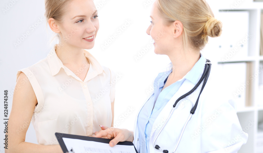 Blonde female doctor and patient talking in hospital office. Health care and client service in medicine Blonde female doctor and patient talking in hospital office. Health care and client service in medicine