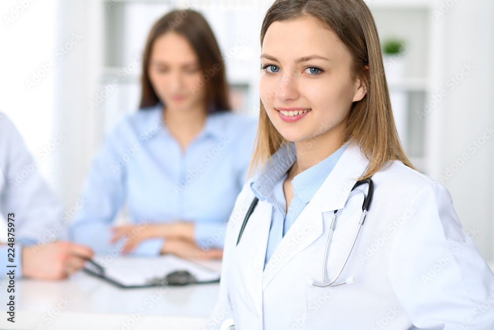 Young beautiful female doctor smiling on the background with patient in hospital Young beautiful female doctor smiling on the background with patient in hospital