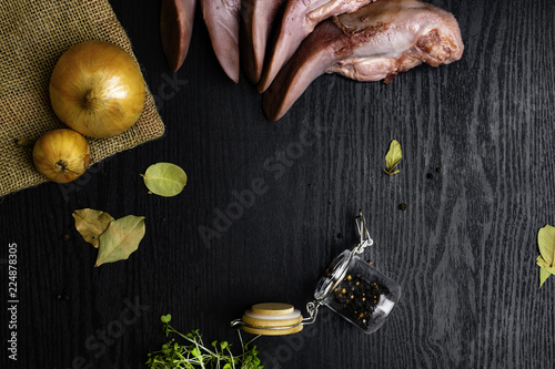 raw pork or beef tongues with black pepper in glass jar, onion on sackcloth, cress salad on black wooden table, gourment food conception photo