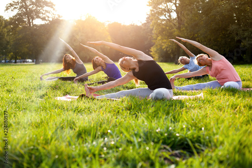 Fototapeta Naklejka Na Ścianę i Meble -  Mixed age group of people practicing yoga outside in the park while sunset