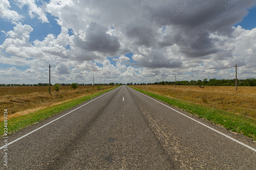 Asphalt road in the steppe and clouds in the blue sky.