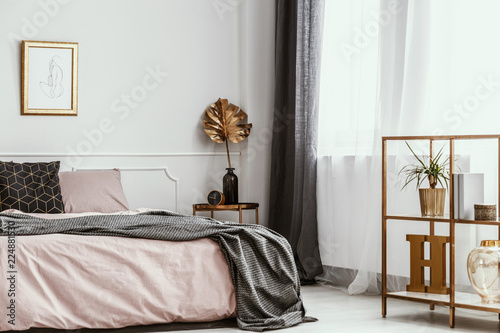Framed silhouette drawing on a white wall of a feminine and artistic bedroom interior with golden decor and pink sheets