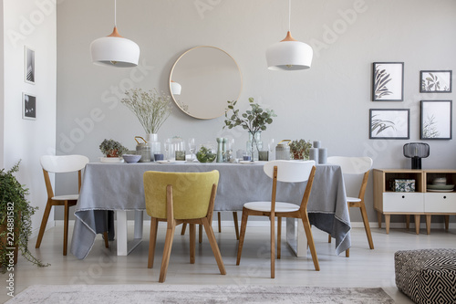 Real photo of an elegant dining room interior with a laid table  chairs  mirror on a wall and lamps