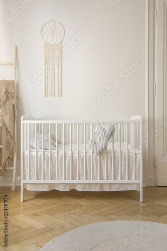 Schilderij op canvas Two heart shaped pillows placed on baby crib standing in white room interior wit
