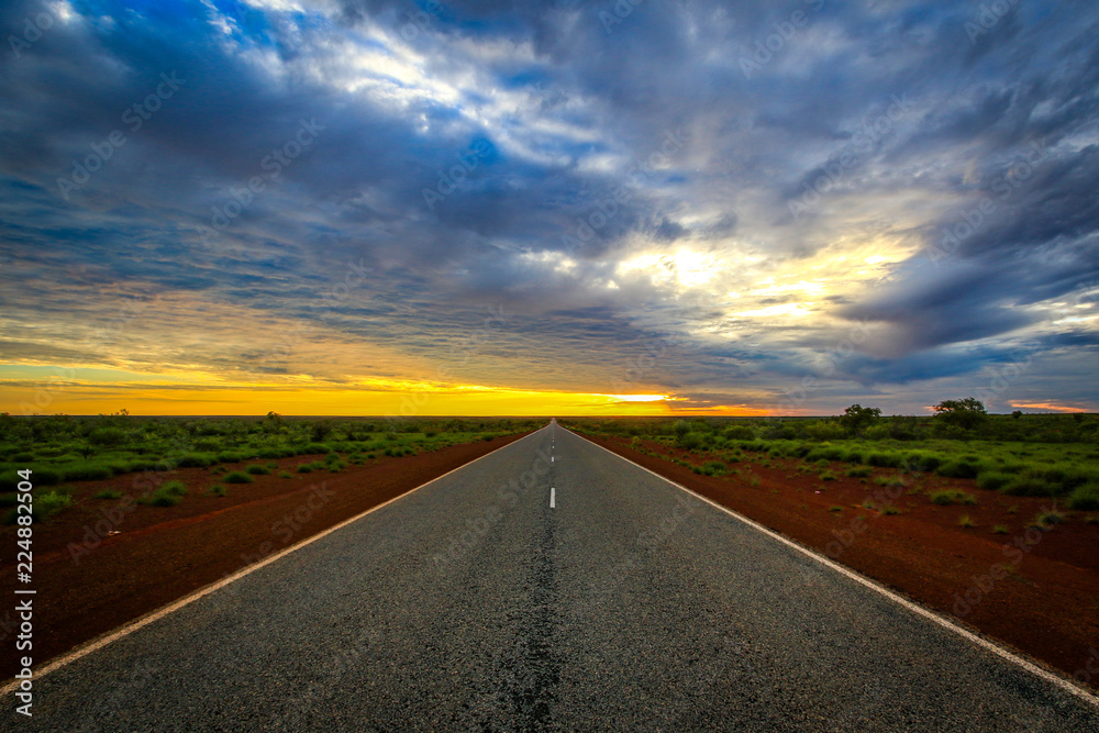 Country road against red dirt leading to dramatic sky 