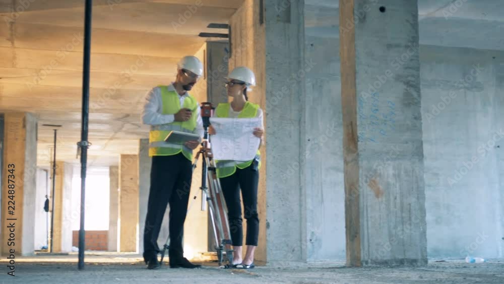 Construction site with two builders, constructors discuss a blueprint. Construction site with two builders, constructors discuss a blueprint.