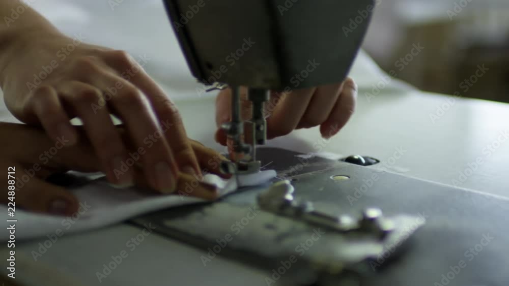 Close up hands of unrecognizable woman learning to make clothes with sewing machine, her colleague helping her Close up hands of unrecognizable woman learning to make clothes with sewing machine, her colleague helping her