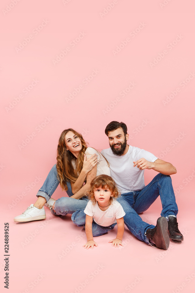 A happy family on pink studio background. The father, mother and son posing together A happy family on pink studio background. The father, mother and son posing together