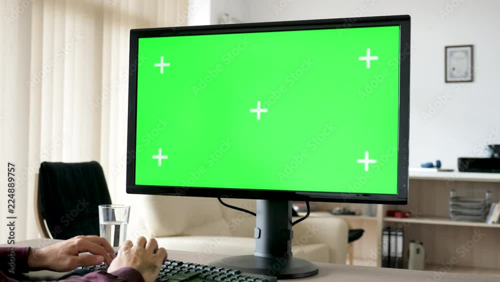 Unrecognisable man typing on personal computer keyboard with big green screen chroma mock-up in the living room of his house. Dolly slider 4K footage with parallax effect
