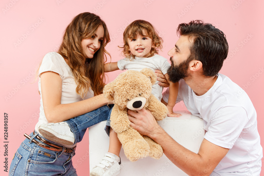 A happy family on pink studio background. The father, mother and son posing together with teddy bear toy A happy family on pink studio background. The father, mother and son posing together with teddy bear toy