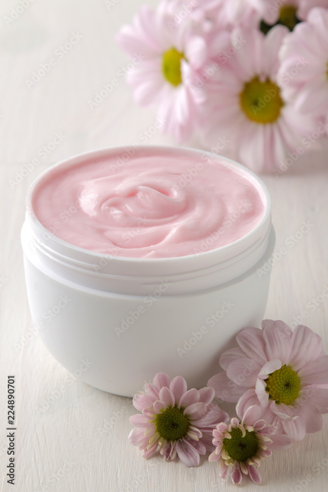 Cream in a white jar close-up and flowers of chrysanthemum on a white wooden table. cosmetics