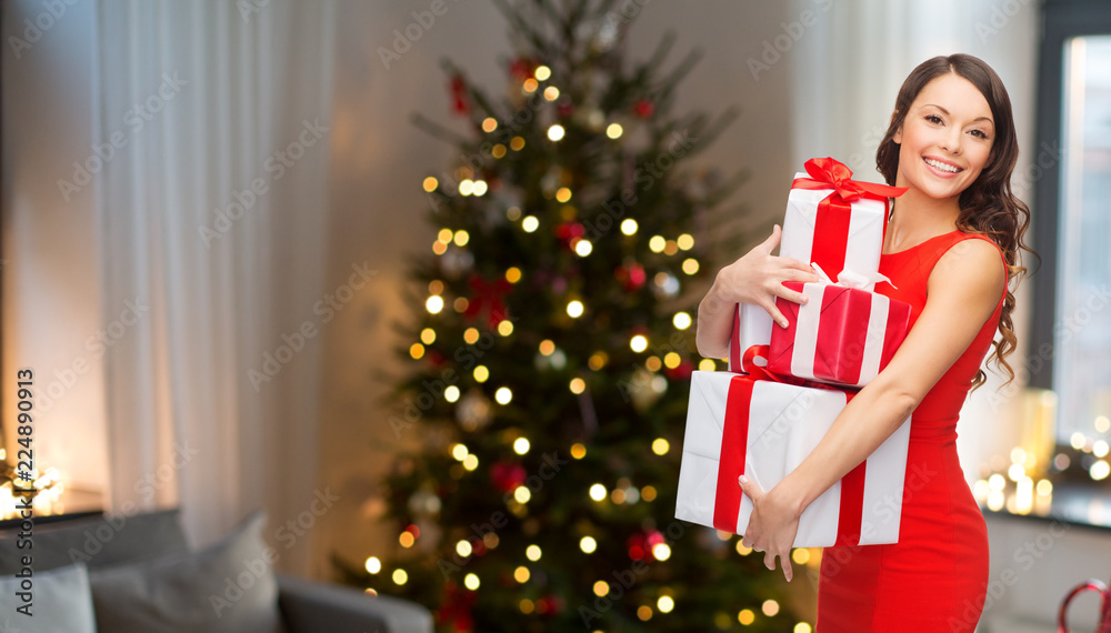 holidays and people concept - smiling woman with gift boxes over living room and christmas tree background holidays and people concept - smiling woman with gift boxes over living room and christmas tree background