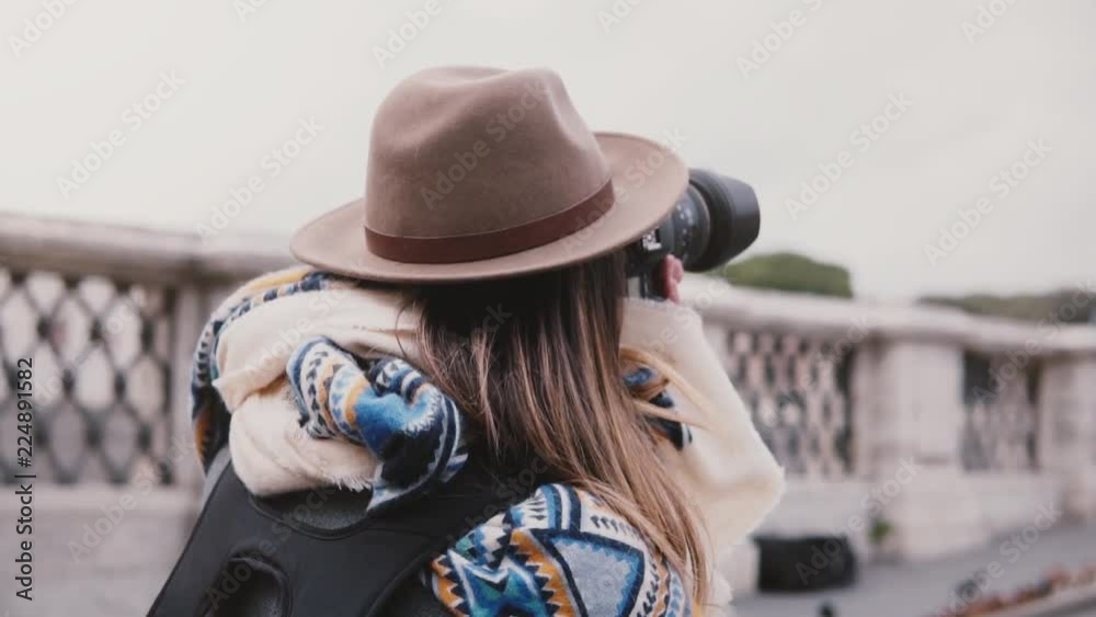 Back view close-up of professional female photographer with backpack in stylish clothes take photo of Rome slow motion.