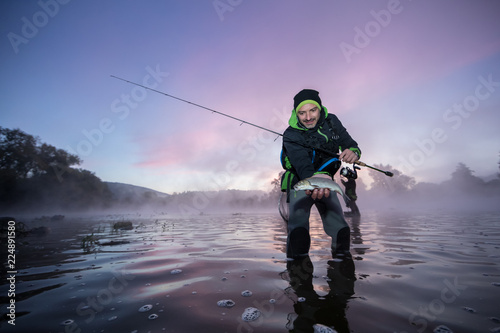 Fisherman holding predatory small fish in river
