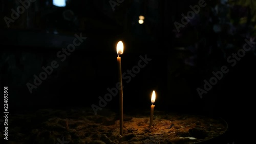 Two wax candles stand in the sand in the Orthodox ancient dark temple photo