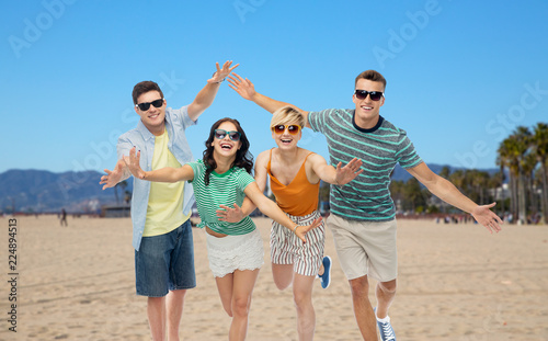 friendship, summer holidays and leisure concept - group of happy smiling friends in sunglasses having fun over venice beach background in california