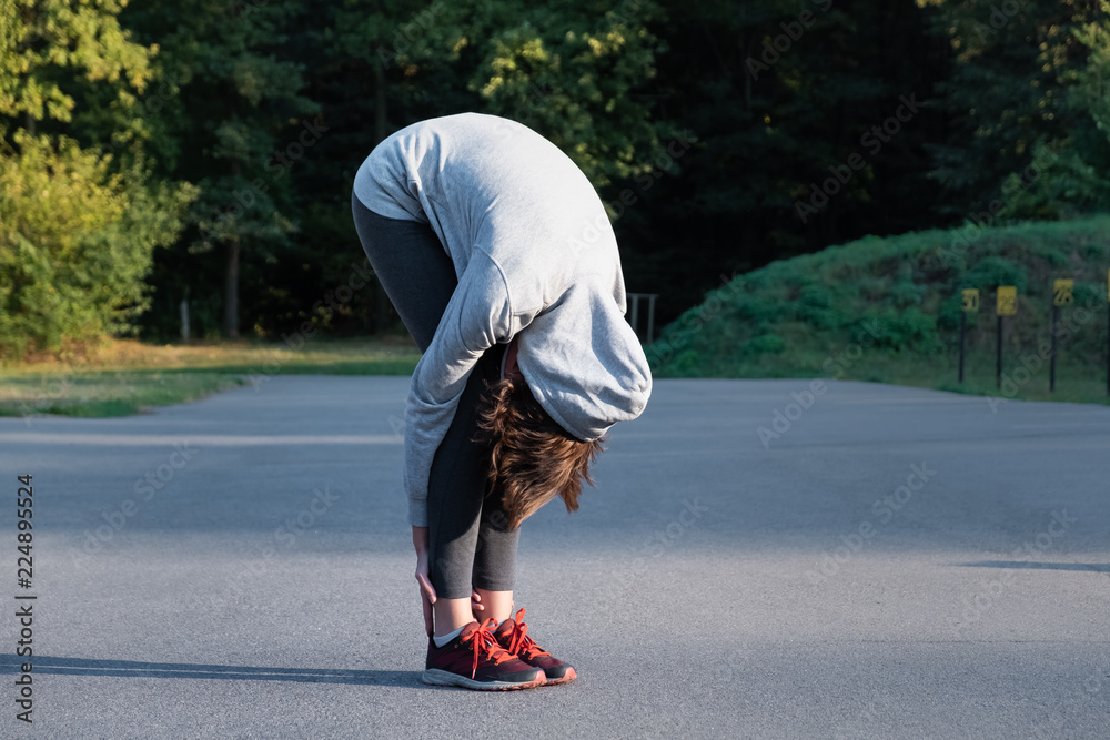 Woman doing beginner yoga excercise for stretching at park. Female person stretching before jogging outdoors Woman doing beginner yoga excercise for stretching at park. Female person stretching before jogging outdoors